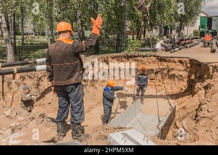 Weißrussland, Region Minsk - 20. Mai 2020: Ein Vorarbeiter in Overalls und ein Schutzhelm steuert den Arbeitsprozess des Hebens von Betonkonstruktionen am Stockfoto