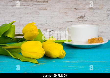 Gelbe Tulpen mit Kaffeetasse auf türkisfarbenem Holztisch Stockfoto