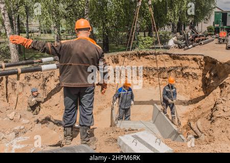 Weißrussland, Region Minsk - 20. Mai 2020: Ein Vorarbeiter in Overalls und ein Schutzhelm steuert den Arbeitsprozess des Hebens von Betonkonstruktionen am Stockfoto