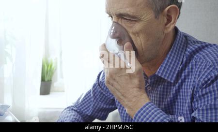 Ein älterer Mann verwendet einen Inhalator. Behandlung von Atemwegsentzündungen mit einem Vernebler. Nahaufnahme. Rehabilitation nach Krankheit Stockfoto