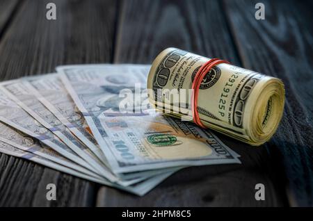 Eine Rolle von Dollarscheinen und Münzen über andere Scheine auf einem Schreibtisch. Highlight für die 100-Dollar-Rechnung. Stockfoto