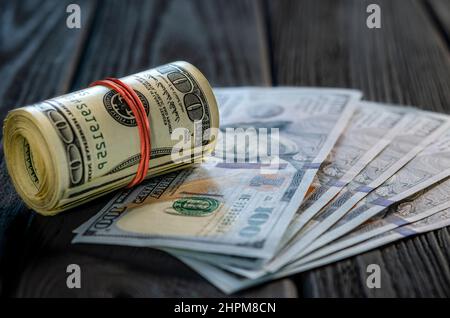 Eine Rolle von Dollarscheinen und Münzen über andere Scheine auf einem Schreibtisch. Highlight für die 100-Dollar-Rechnung. Stockfoto