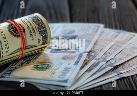 Eine Rolle von Dollarscheinen und Münzen über andere Scheine auf einem Schreibtisch. Highlight für die 100-Dollar-Rechnung. Stockfoto