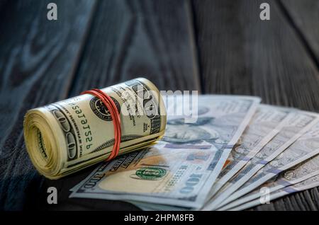 Eine Rolle von Dollarscheinen und Münzen über andere Scheine auf einem Schreibtisch. Highlight für die 100-Dollar-Rechnung. Stockfoto