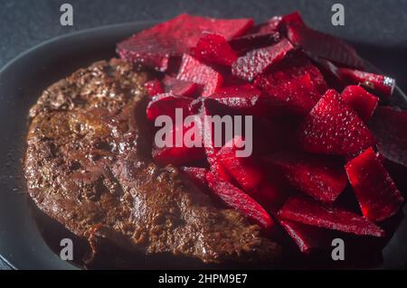 Gebratene Ochsenleber mit Rote Bete und auf einen schwarzen Teller mit Zwiebeln gelegt, Kopierplatz links, brasilianisches Essen. Stockfoto