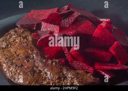 Gebratene Ochsenleber mit Rote Bete und auf einen schwarzen Teller mit Zwiebeln gelegt, Kopierplatz links, brasilianisches Essen. Stockfoto