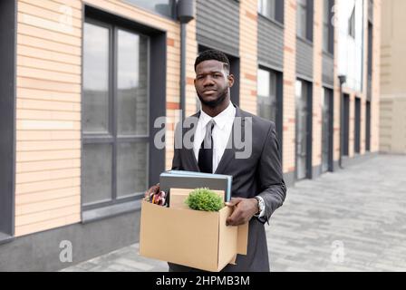 Gefeuert afroamerikanischen männlichen Büroangestellte mit Box mit persönlichen Sachen verloren Job und ging ohne Geld nach Hause Stockfoto