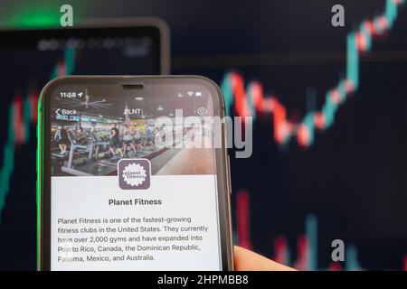 Der Aktienkurs von Planet Fitness steigt am Handelsmarkt mit einem Balkendiagramm im Trenddiagramm im Hintergrund. Mann mit Mobiltelefon und Firmenlogo, Februar 2022, San Francisco, USA Stockfoto