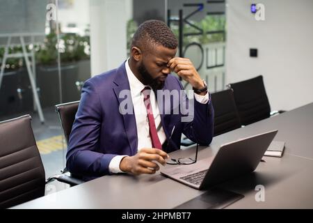 Erschöpfter schwarzer Manager sitzt im Büro und hat Kopfschmerzen Stockfoto