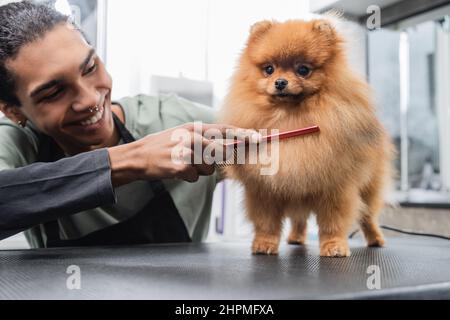Junger afroamerikanischer Mann lächelt, während er im Friseursalon spitz putzt Stockfoto