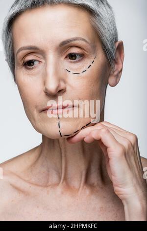 Reife Frau mit Falten und markierten Linien im Gesicht isoliert auf grau Stockfoto