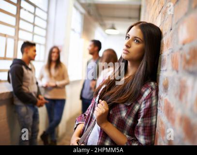 Das Leben auf dem Campus lieben. Aufnahme einer schönen jungen Studentin, die gelangweilt aussieht, während sie sich auf dem Campus an eine Ziegelsteinmauer lehnt. Stockfoto