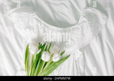 Sommerkleid aus weißer Baumwolle und Blumenstrauß aus Tüll. Draufsicht. Konzept des Frühlings-, Sommer-Outfits. Stillleben. Minimalkonzept. Speicherplatz kopieren Stockfoto