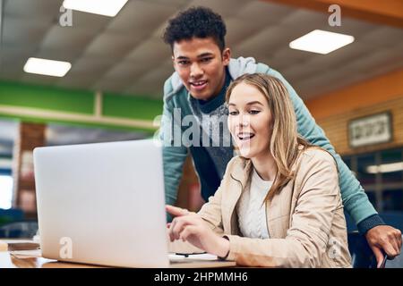 Hier finden Sie alle Informationen auf Knopfdruck. Aufnahme eines jungen Mannes, der anschaut, während eine Studentin an einem Laptop arbeitet. Stockfoto