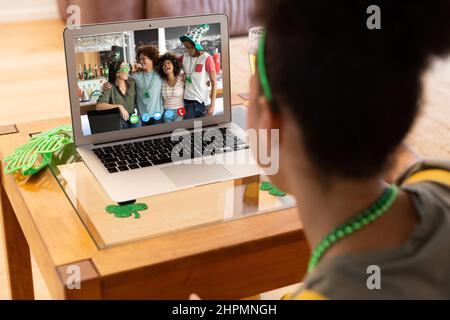 Frau mit gemischtem Rennen, die zu Hause mit einer Gruppe von Freunden einen Videoanruf zum St. patrick's Day auf einem Laptop führt Stockfoto