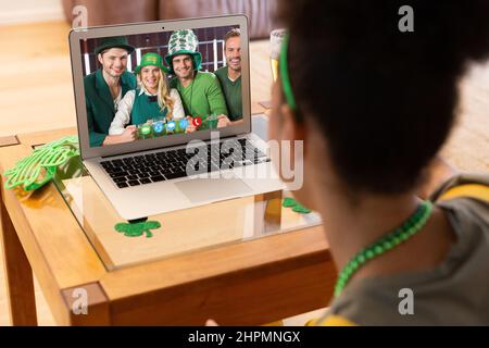 Frau mit gemischtem Rennen, die zu Hause mit einer Gruppe von Freunden einen Videoanruf zum St. patrick's Day auf einem Laptop führt Stockfoto