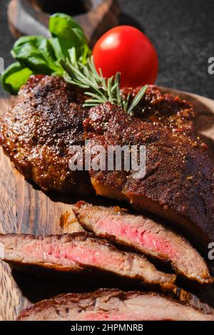 Nahaufnahme der in einer gusseisernen Pfanne gebratenen Rinderspinne, serviert auf einem Holzschneidebrett mit Tomaten und Basilikum Stockfoto