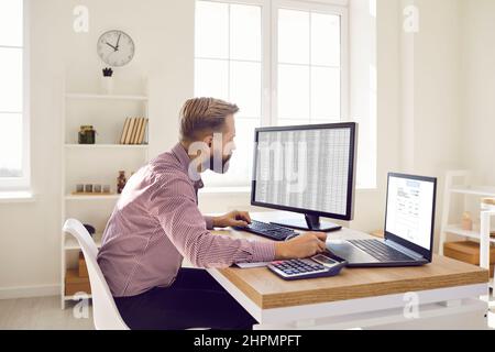 Buchhalter sitzt am Schreibtisch und arbeitet mit Kalkulationstabellen und Rechnungen auf Computern Stockfoto