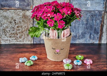Blumentopf mit Hasengesicht und kleinen Stoffblumen im Fokus. Stockfoto
