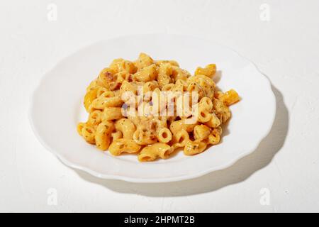 Lockige Pasta mit Sauce auf einem weißen Teller. Minimalismus. Weißer Hintergrund. Pasta in Käsesauce. Stockfoto