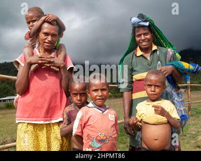 Zwei Frauen und vier Kinder im Hochland PNG. Zwei Jungen haben Hemden hochgezogen, die vergrößerte Bäuche von entweder Kwashiorkor oder Splenomegalie zeigen. Stockfoto