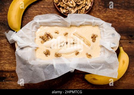 Ungekochte Teig Bananenbrot in der Form. Kochen. Holzhintergrund. Blick von oben. Süßes, vegetarisches Essen. Stockfoto