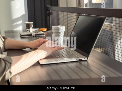 Weibliche Hände Nahaufnahme Text auf Laptop-Tastatur eingeben. Frau, die am Kaffeetisch mit Computer und Kaffeetasse sitzt. Digitale Technologien im Arbeits-, Bildungs- und Sozialkommunikationskonzept. Foto Stockfoto