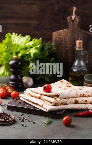 Lavasch gerollt auf einem Holzbrett, dünnes traditionelles orientalisches Brot, armenisches Fladenbrot, Gemüse, Käse, Gemüse und Sauce, Rustikaler Hintergrund Stockfoto