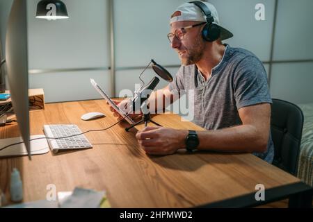 Blogger im mittleren Alter mit Kopfhörern, der Text aufzeichnet oder Online-Webinare oder Nachrichtenankündigungen macht. Moderner Home Sound Studio-Audiorecor Stockfoto