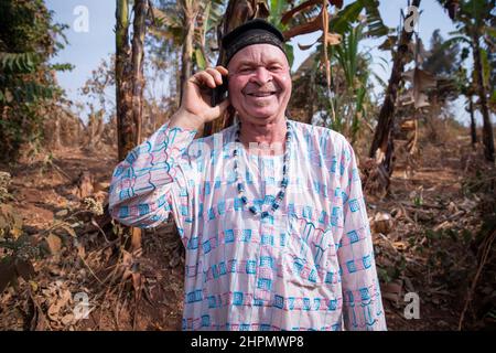 Afrikanischer Albino-Senior telefoniert und ist glücklich. Mann mit Albinismus-Syndrom in traditioneller afrikanischer Kleidung. Stockfoto