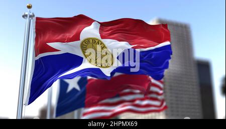 Die Stadtflagge von Dallas winkt im Wind, während die Nationalflaggen von Texas und den Vereinigten Staaten im Hintergrund verschwommen sind Stockfoto