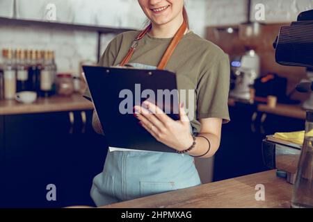 Lächelnde Barista, die im Café auf die Zwischenablage schrieb Stockfoto