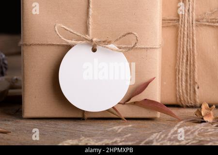 Runde weiße Geschenkanhänger Mockup an Weihnachten oder Valentinstag verpackt Geschenke auf rustikalem Holzhintergrund mit Boho Dekoration. Federleeretikett Produ Stockfoto