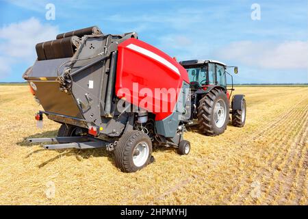 Ein landwirtschaftlicher Traktor mit Anhängevorrichtung zum Sammeln von Stroh vom Feld und zur Lagerung in Ballen. Stockfoto