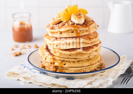 Pfannkuchen. Hausgemachter flauschiger Pfannkuchen mit Banane, Walnuss und Karamell zum Frühstück auf hellem Betongrund. Leckere Pfannkuchen für traditionelle Gerichte Stockfoto