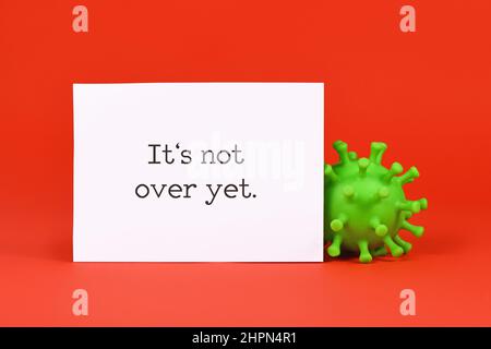 Corona-Virusmodell und Anmerkung mit dem Text „IT's Not Over Yet“ auf rotem Hintergrund Stockfoto