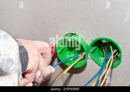 Ein Elektriker installiert eine Steckdose in einer Trockenwand, um eine Steckdose zu installieren. Renovierung des Hauses. Stockfoto