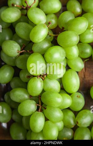 Ein Bild von frisch geernteten rohen grünen Bio-Trauben, die auf einem rustikalen Holztisch sitzen. Stockfoto