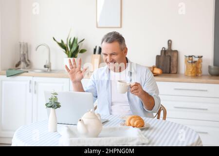 Älterer Mann mit einer Tasse Tee Video chattet am Tisch in der Küche Stockfoto