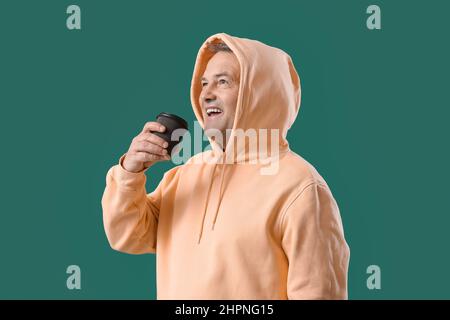 Älterer Mann im Hoodie mit einer Tasse Kaffee auf grünem Hintergrund Stockfoto