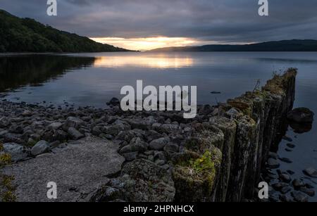 Blick auf Loch Rannoch über den Pier am Ostufer, während die Sonne über den Bergen in der Ferne untergeht, Rannoch, Schottland, Vereinigtes Königreich. Stockfoto