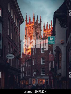 Das York Minster badete in einem warmen Abendlicht und ragte über den roten Backsteinläden von Low Petergate Stockfoto