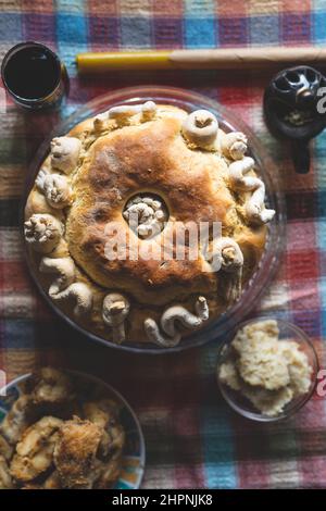 Der Familienvater hält die Feier des schutzpatrons Ein hausgemachtes Slava-Kuchenbrot von oben auf dem Tisch, um traditionelle Gerichte zu feiern, die für einen orthodoxen Urlaub zubereitet werden Stockfoto