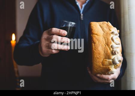 Der Familienvater hält die Feier des schutzheiligen Ein hausgemachtes Slava-Kuchenbrot in Menschenhänden mit Wein, um traditionell für orthod zubereitet zu feiern Stockfoto