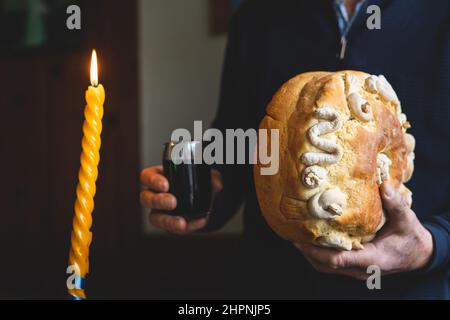 Der Familienvater hält die Feier des schutzheiligen Ein hausgemachtes Slava-Kuchenbrot in Menschenhänden mit Wein, um traditionell für orthod zubereitet zu feiern Stockfoto