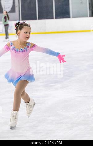 Kleines Mädchen, das Eiskunstlauf auf einer Indoor-Eisbahn übt. Stockfoto