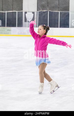 Kleines Mädchen, das Eiskunstlauf auf einer Indoor-Eisbahn übt. Stockfoto