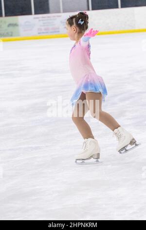 Kleines Mädchen, das Eiskunstlauf auf einer Indoor-Eisbahn übt. Stockfoto