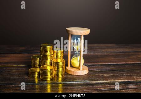 Geldmünzen und Sanduhr. Faire Stundenlöhne. Zeit ist Geld. Anzahlung. Rentabilität und Investitionsrendite. Balance zwischen Leben und Karriere. Stockfoto