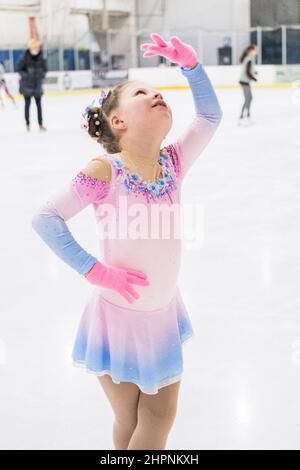 Kleines Mädchen, das Eiskunstlauf auf einer Indoor-Eisbahn übt. Stockfoto